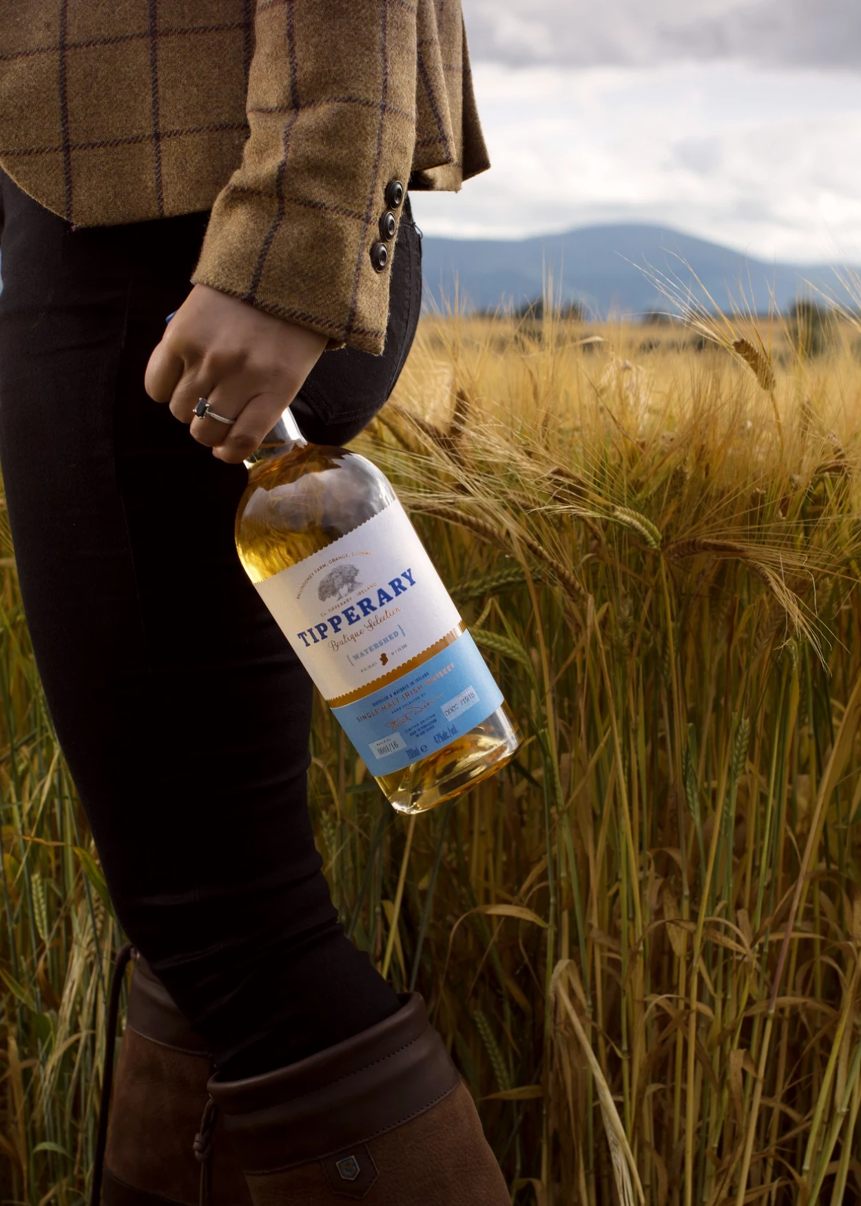 Jennifer in a field holding a bottle of Watershed whiskey 
