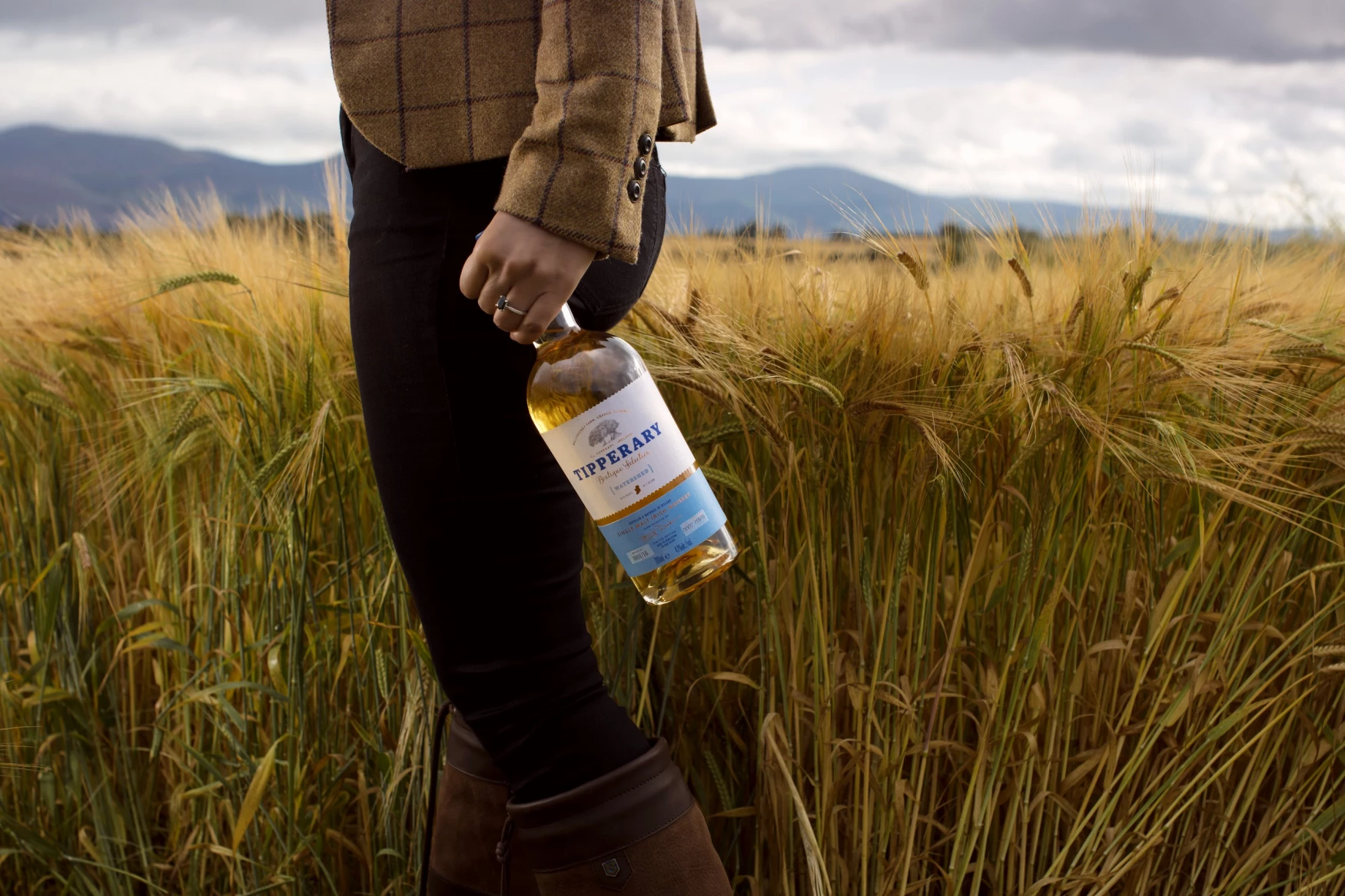 Jennifer in a field holding a bottle of Watershed whiskey 