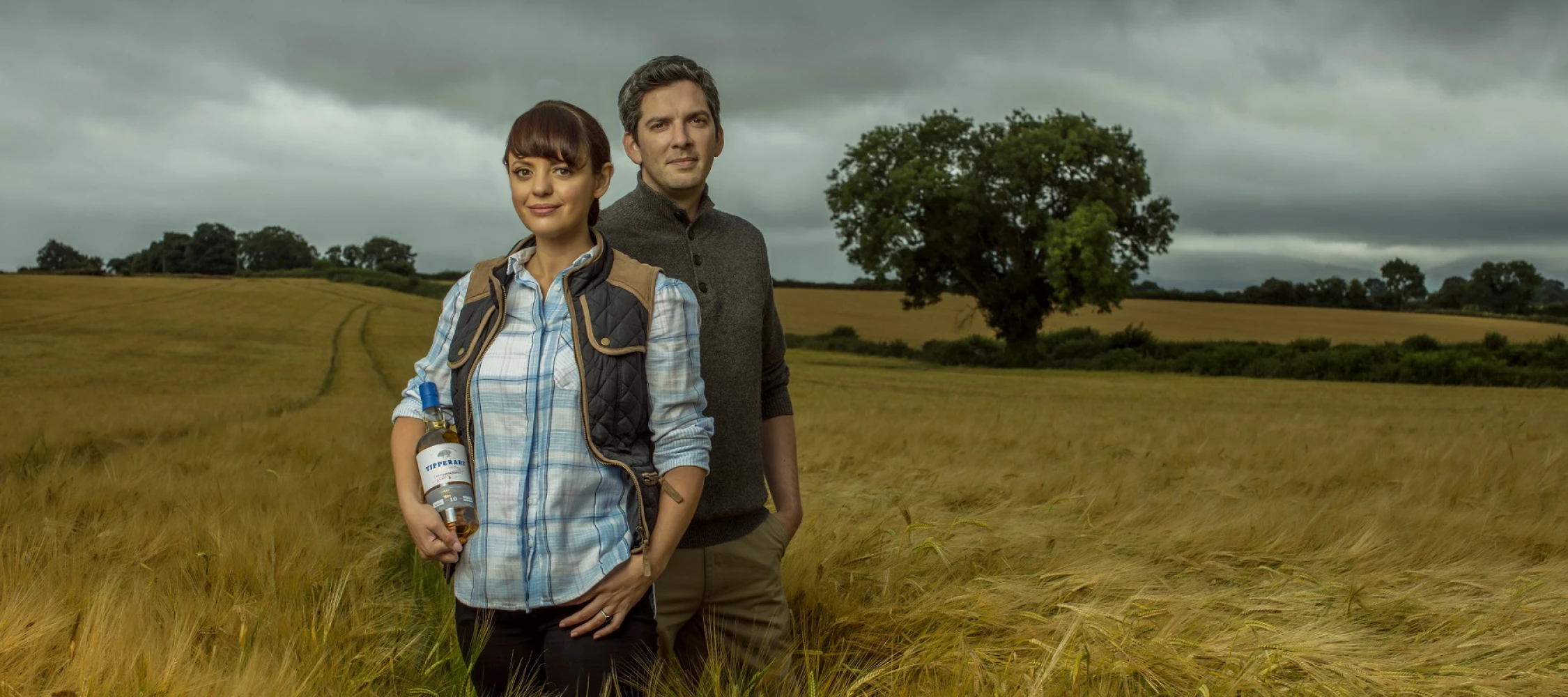 Jennifer and Liam in a field holding a bottle of Watershed whiskey 