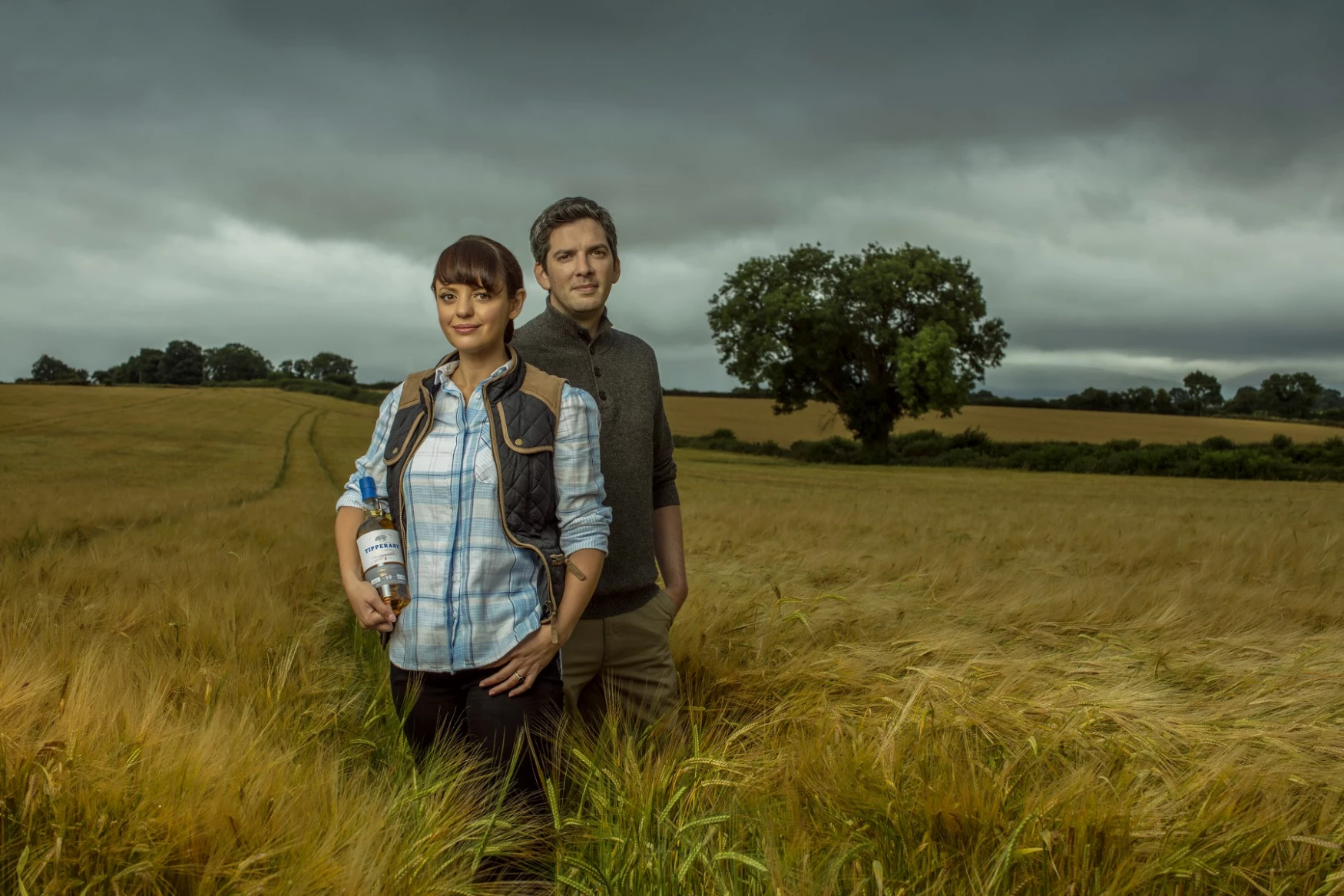 Jennifer and Liam in a field holding a bottle of Watershed whiskey 